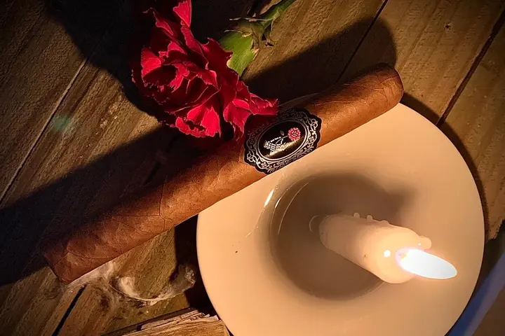 Un cigarro junto a un clavel rojo y una vela encendida